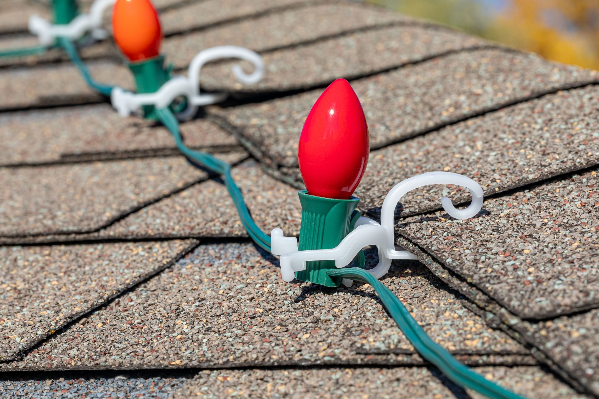 Hanging Christmas string lights on shingles of roof. Holiday decorating safety, lighting and accident prevention concept.