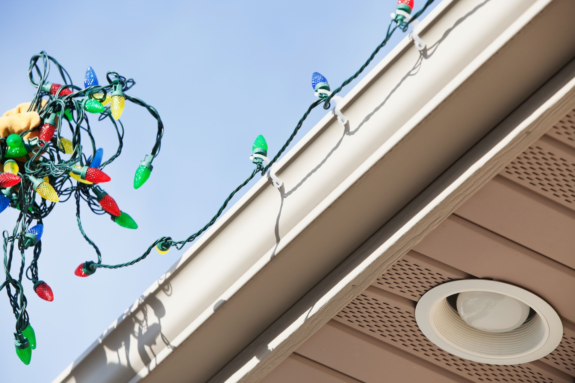 Gloved Hand Installing LED Christmas Lights on House Rain Gutter